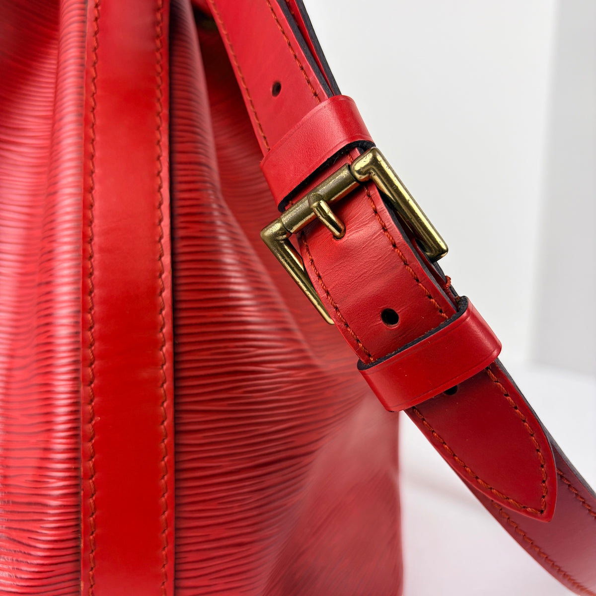 Red shoulder strap with gold buckle and stitched leather belt attachment