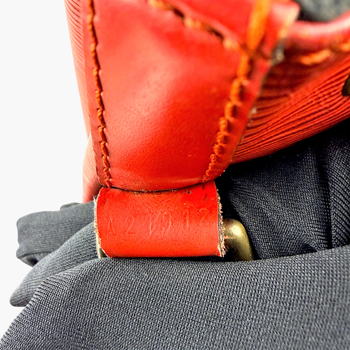 Red leather strap end with stitching and worn edge showing attachment hardware