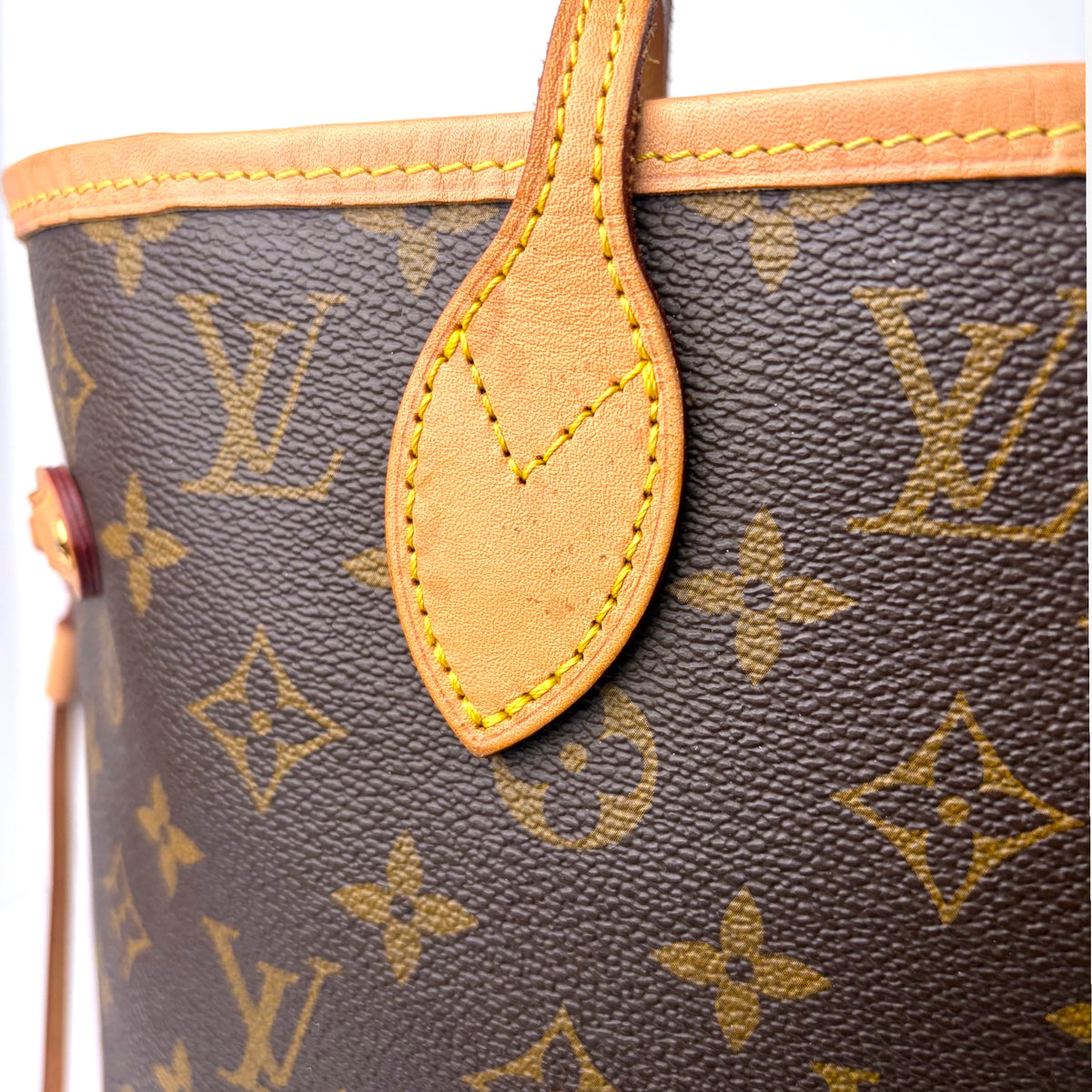 Monogram tote bag close-up of tan teardrop pull tab against patterned canvas
