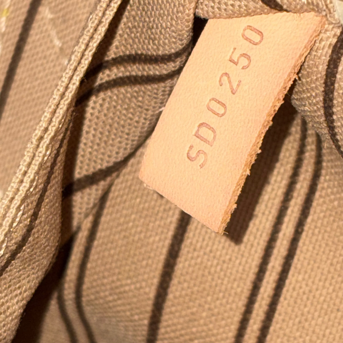 Brown monogram fabric close-up with stitched seam and light leather authenticity tag