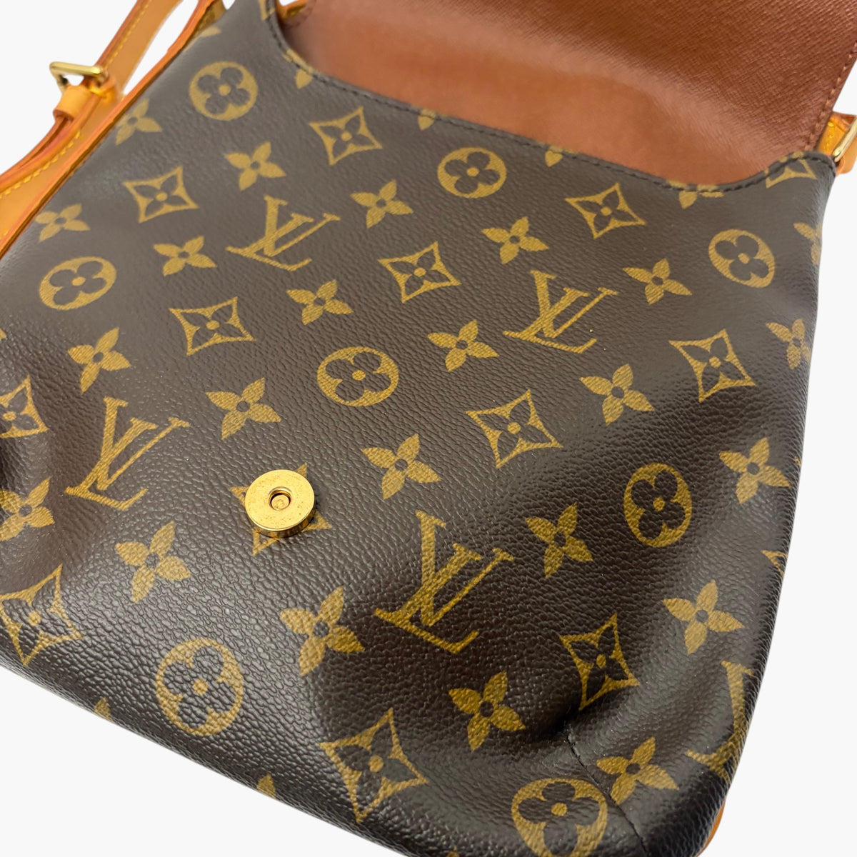 Monogram crossbody bag close-up, tan snap button on dark patterned leather exterior