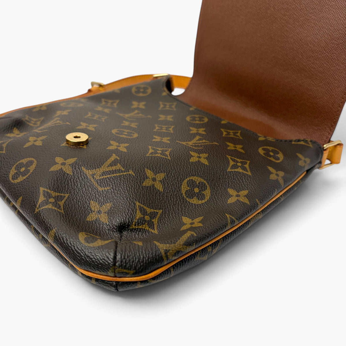 Monogram crossbody bag base close-up, dark patterned exterior with tan snap hardware