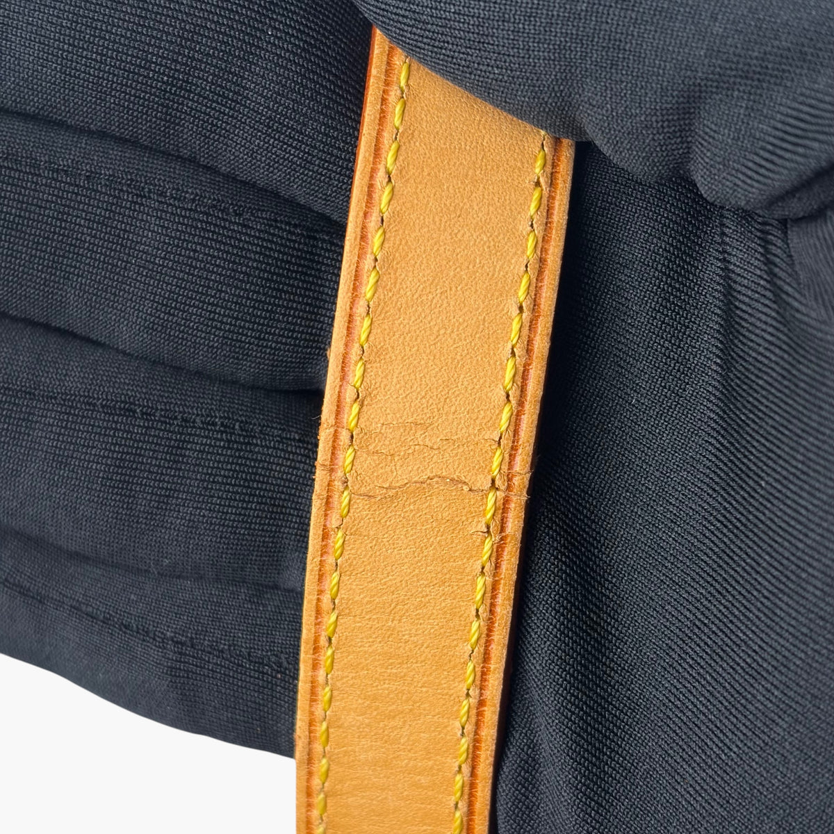 Crossbody bag strap attachment detail, tan leather patch with yellow stitching on dark