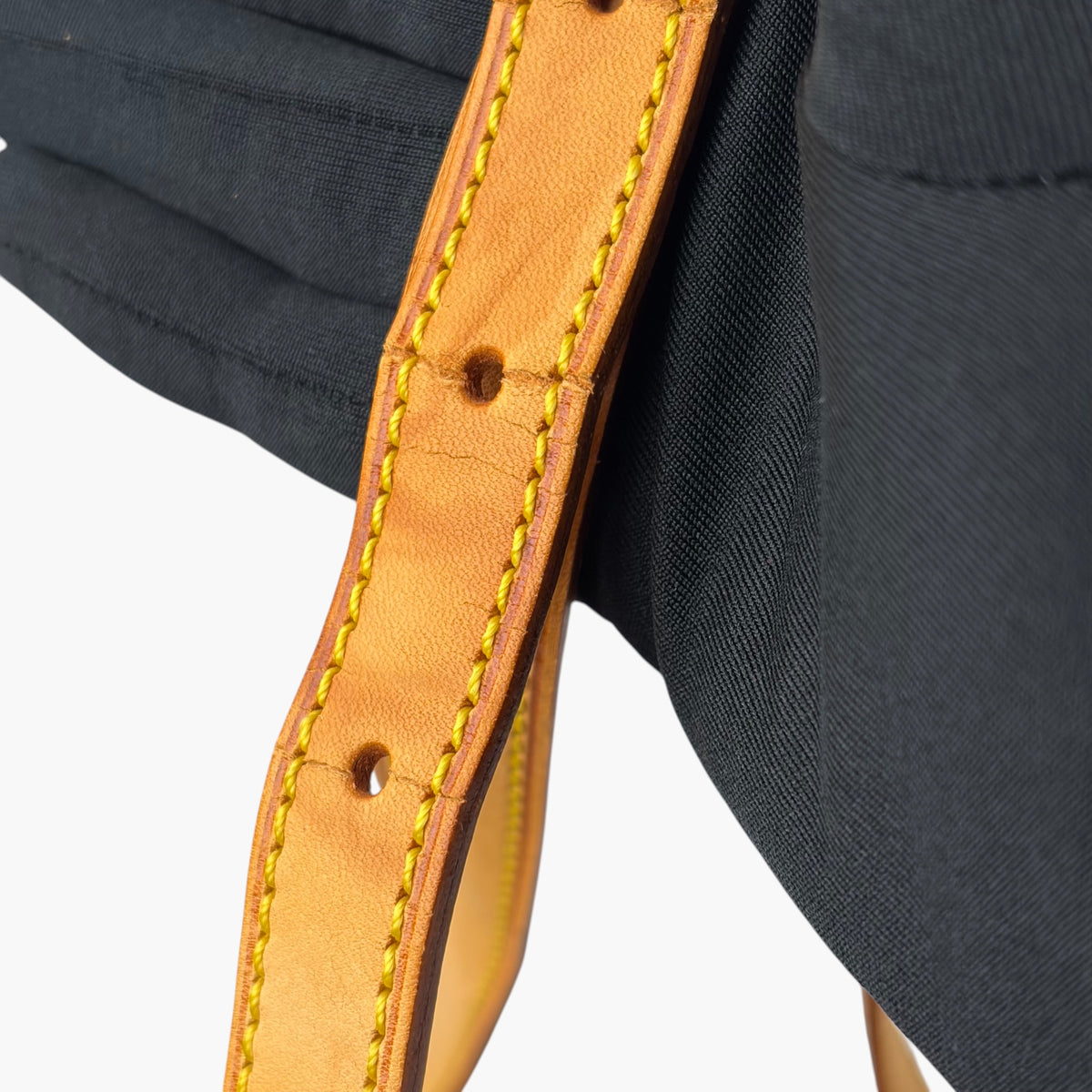 Tan leather bag strap with gold-stitched holes and rivets on dark fabric