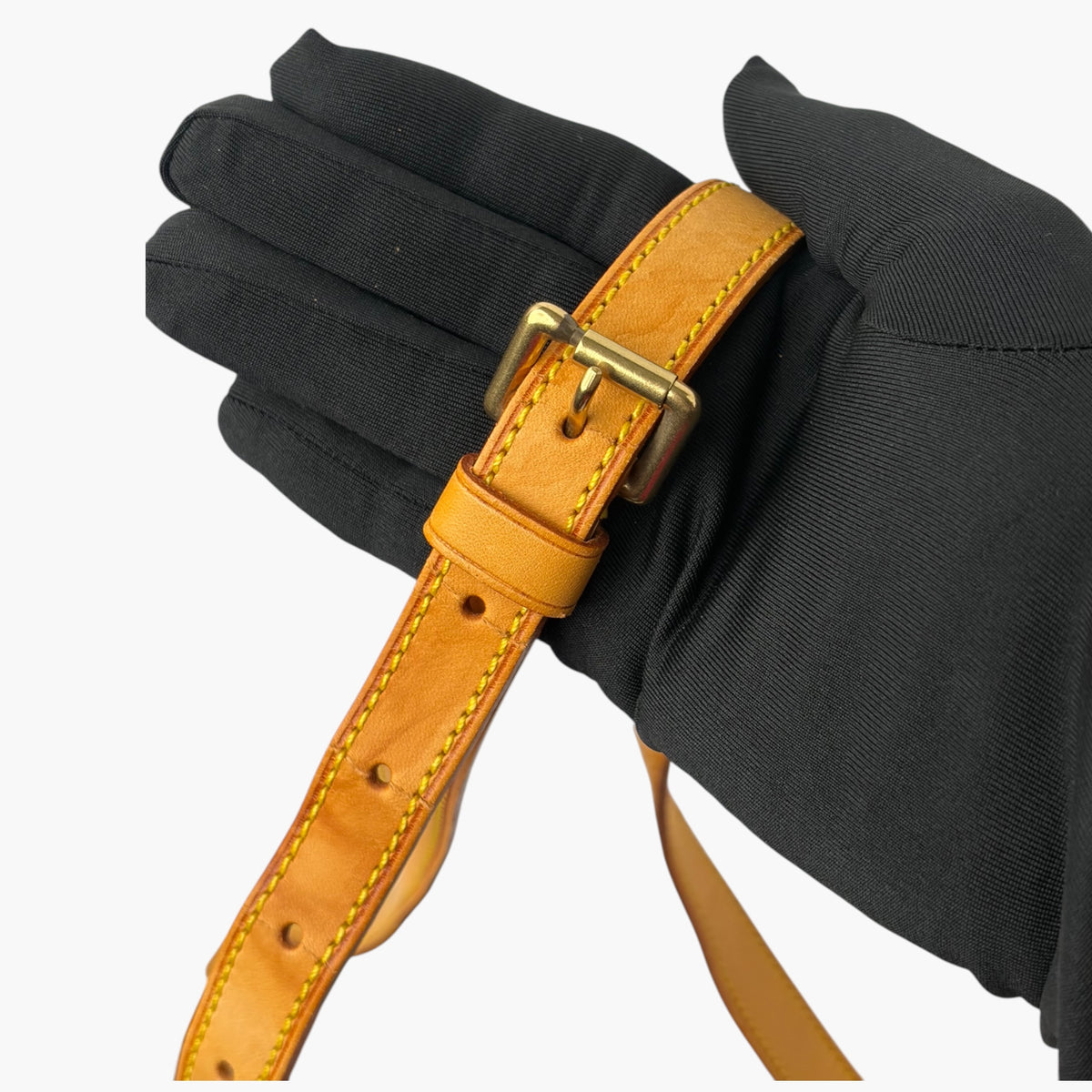 Tan leather long strap with brass buckle and grommet details on dark fabric