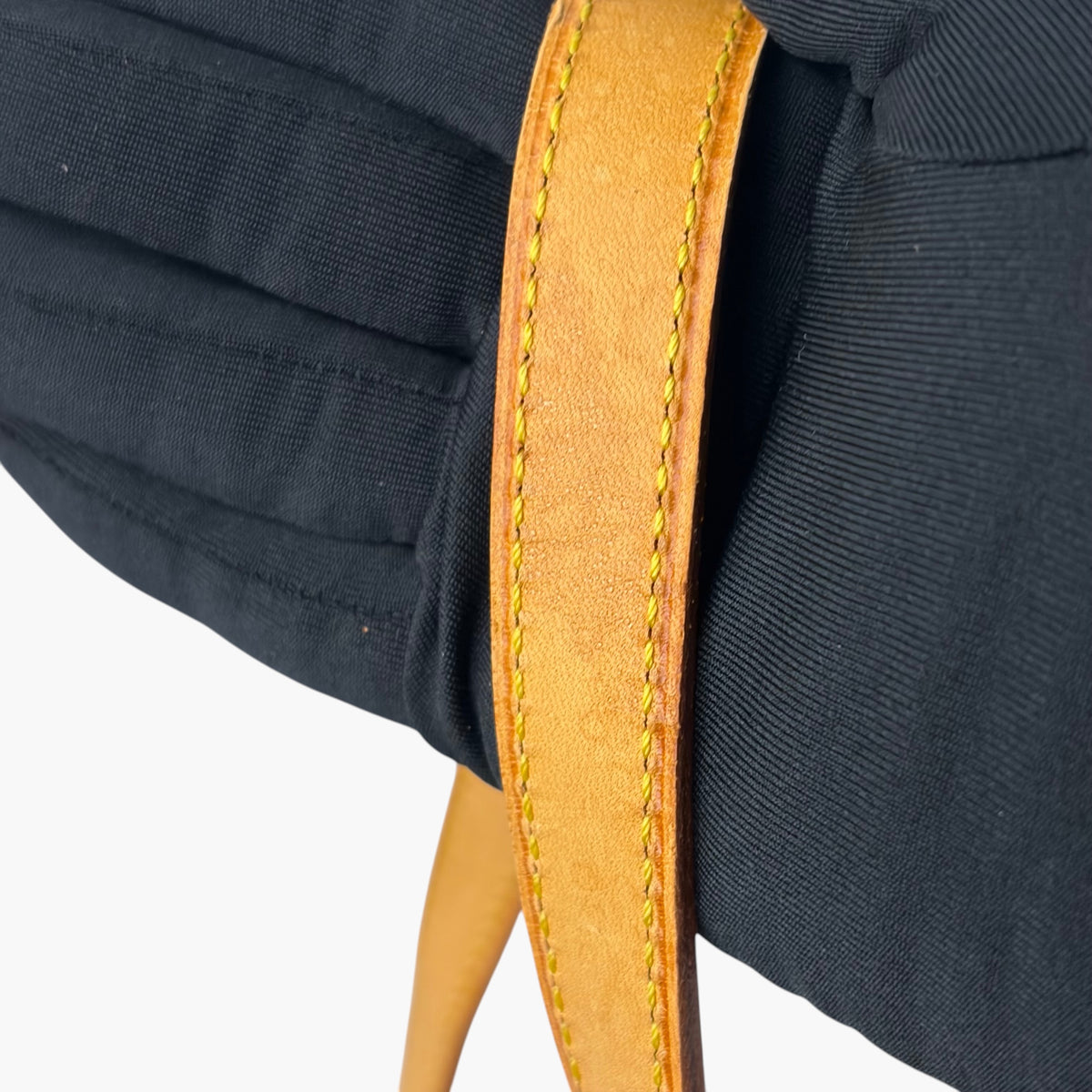 Tan leather strap edge with gold stitching on dark bag panel