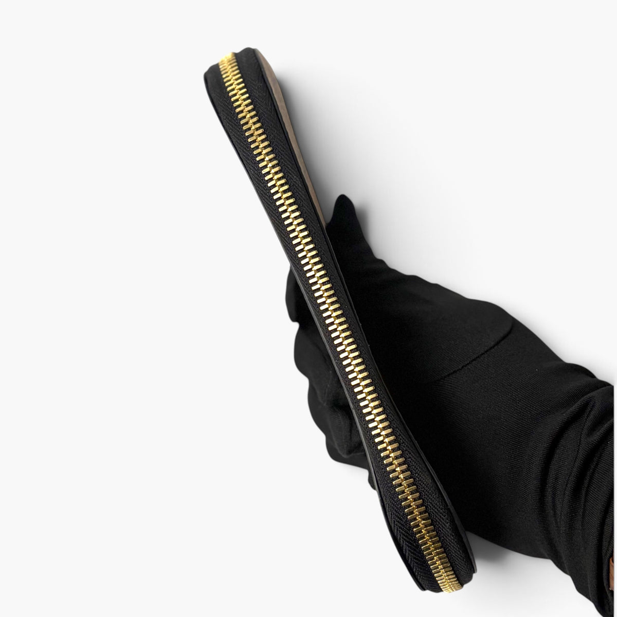 Black pencil case held in glove, showing gold-tone zipper track