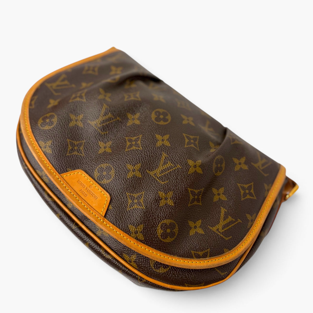 Monogram canvas flap bag angled view with tan leather piping and stitched edges.