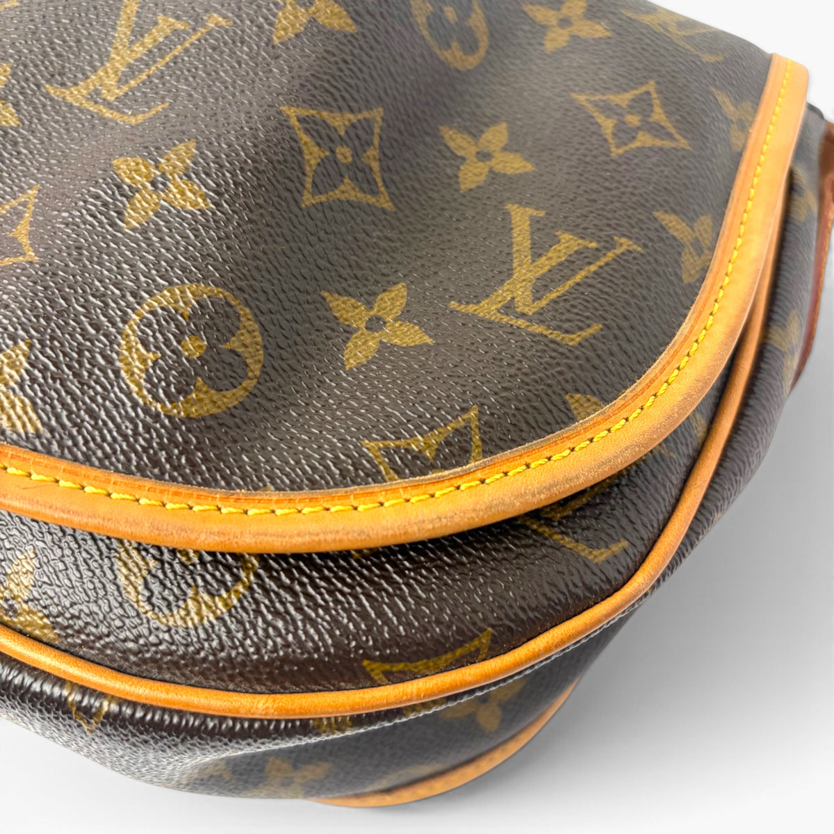 Close-up of monogram canvas flap edge with tan leather trim and double stitching.