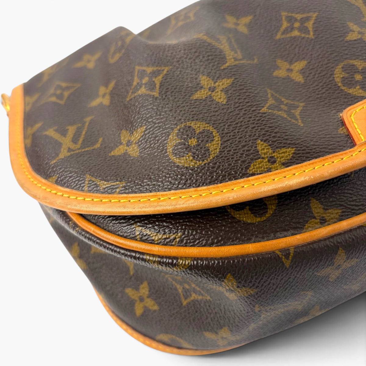 Monogram canvas bag corner view with tan leather trim and stitched flap border.