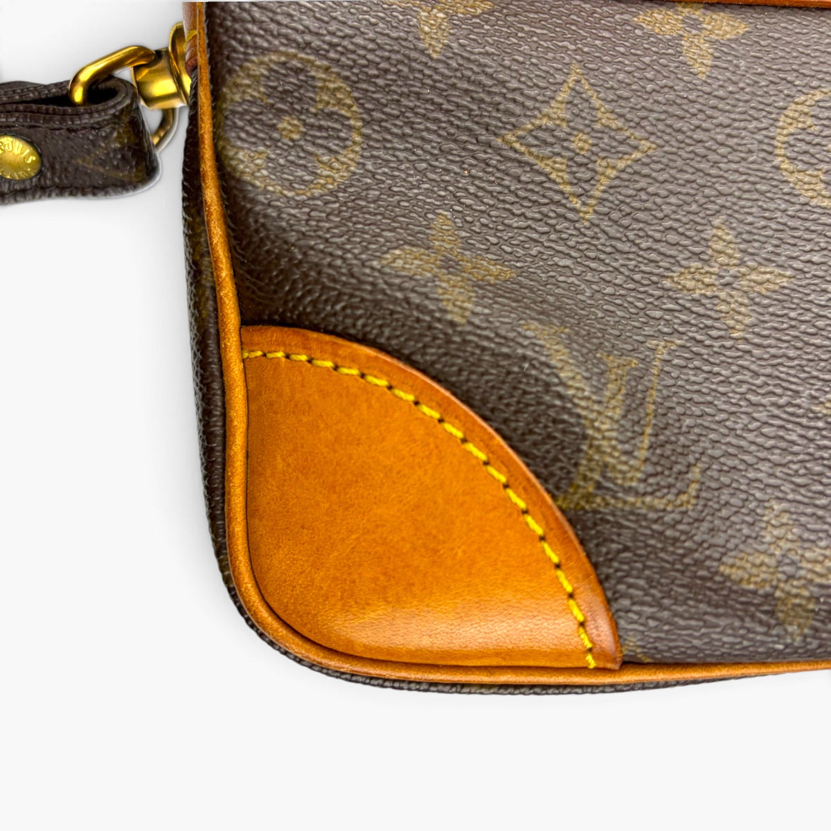 Monogram pouch corner with tan leather panel, gold ring, and zipper pull