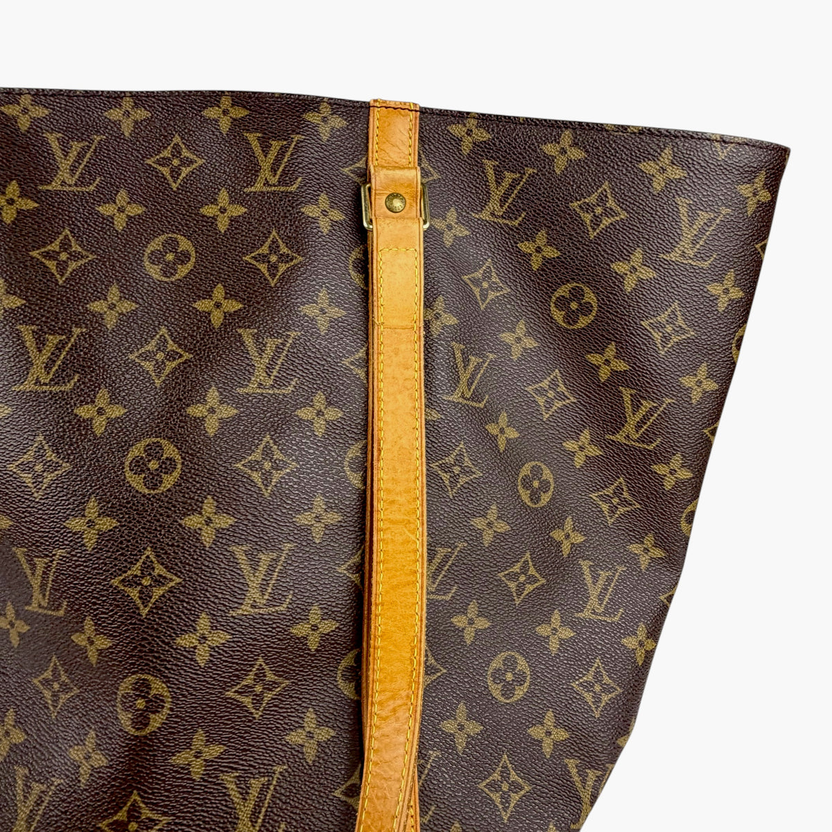 Brown monogram tote bag detail with tan center strap and metal rivet