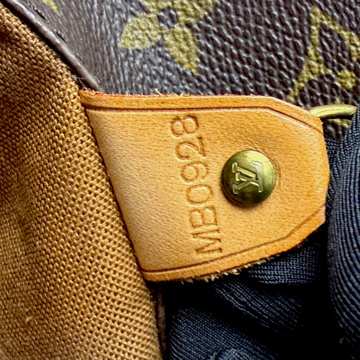 Tan leather brand patch with snap button on monogram tote bag